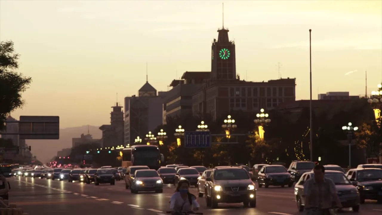 Heavy traffic flowing on a Chinese city road with a landmark clock tower at sunset