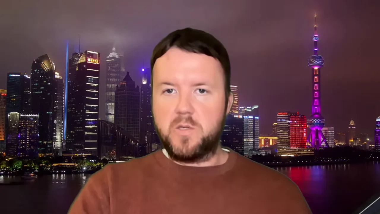 Presenter speaking with Shanghai skyline background, linking Iran fallout to cost pressures on China’s factories