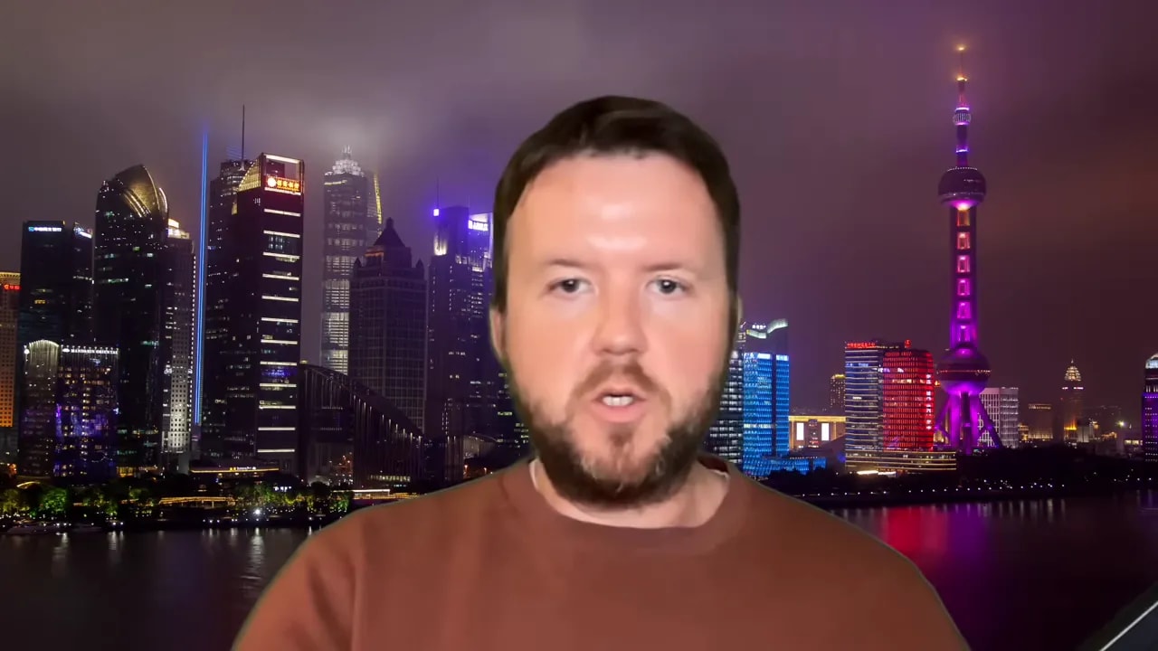 Presenter on camera explaining geopolitical developments with neon-lit skyline background